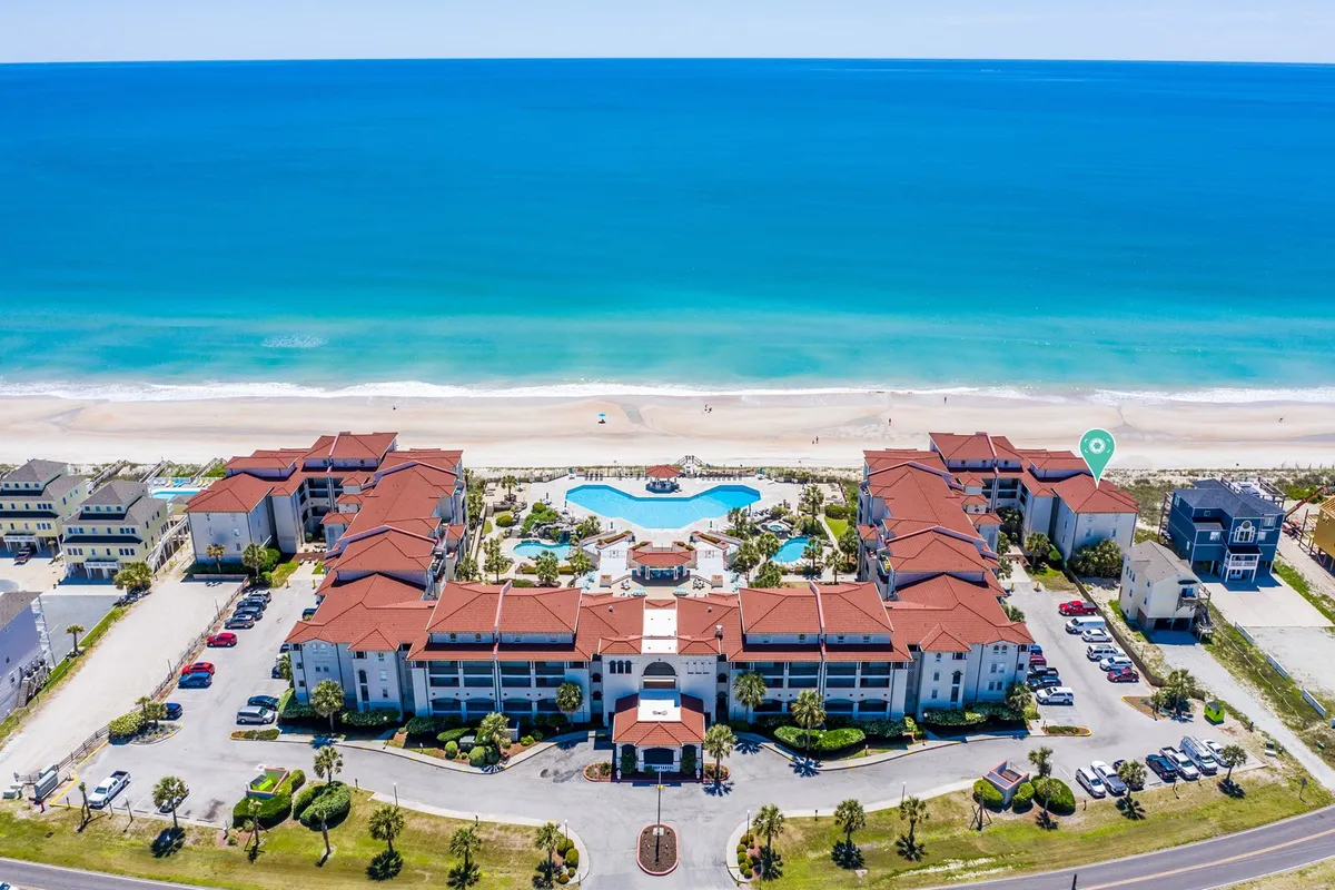 This image captures an inviting exterior scene featuring a beachfront swimming pool surrounded by landscaped gardens and the architectural elements of Villa Capriani's buildings. The ocean is visible just beyond the pool, and the space is designed for both relaxation and social gatherings.