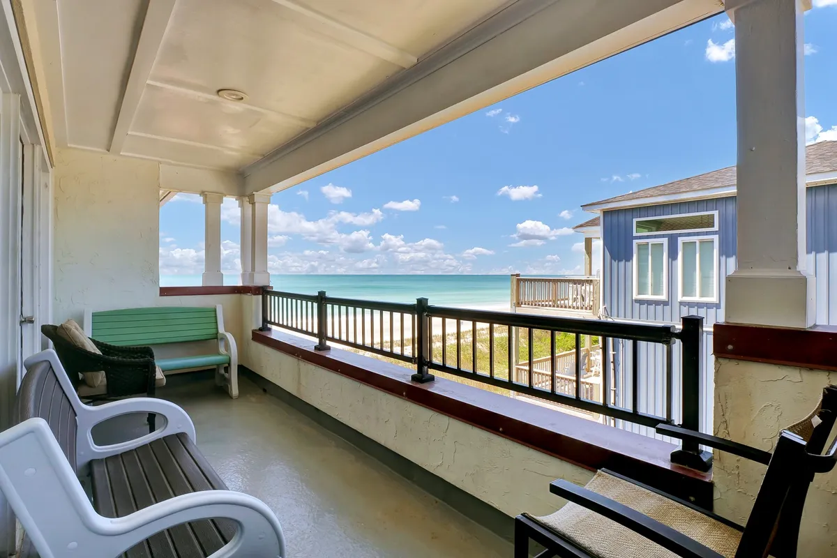 An exterior shot from the balcony itself, featuring comfortable seating, the balcony railing, and a stunning view of the ocean. The tranquil setting is perfect for enjoying a morning coffee or watching the sunset as waves crash below.