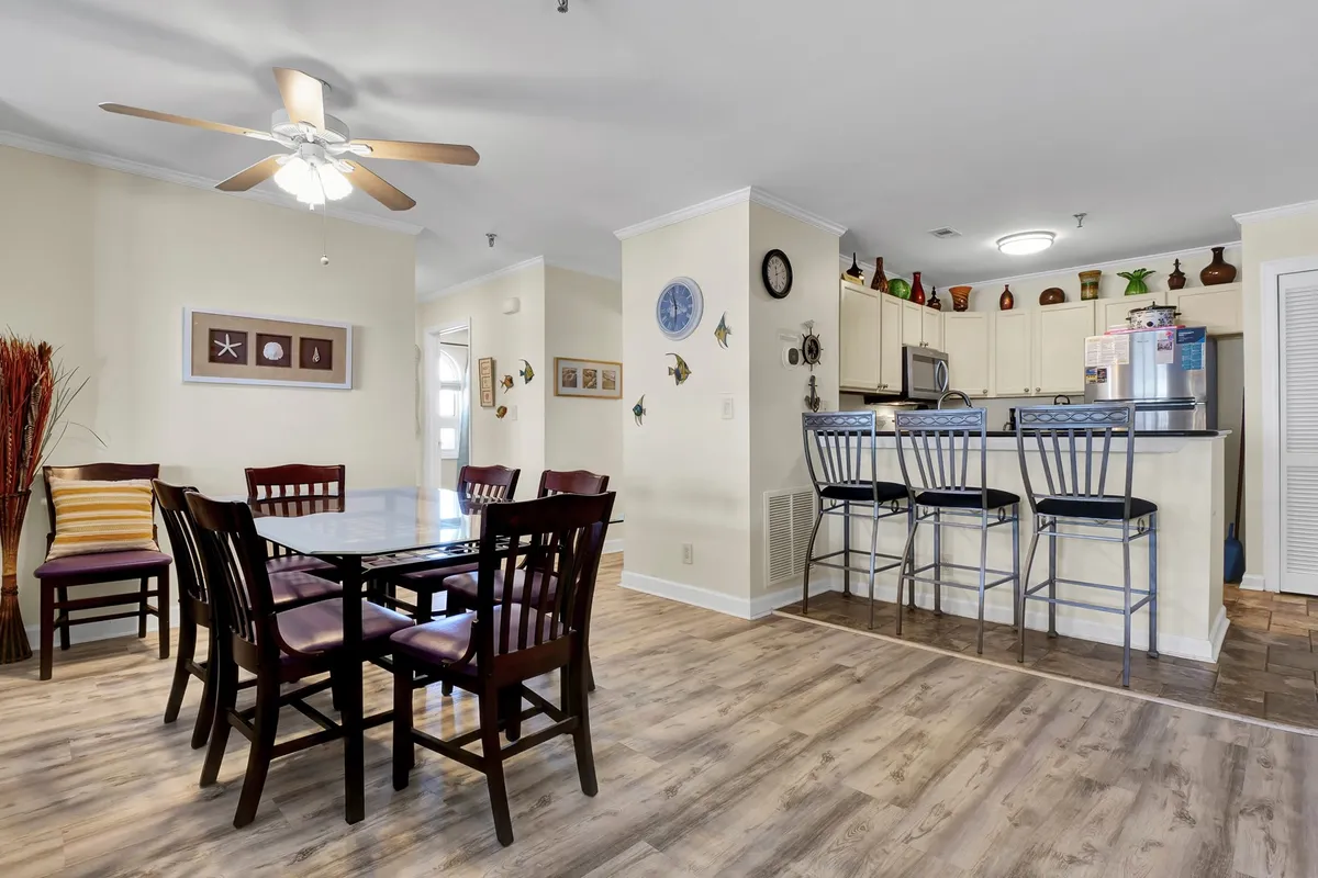 This image features a dining table and chairs set against a backdrop of the kitchen bar area, with decorative wall art adding warmth to the scene. The setup is ideal for shared meals, celebrations, and gatherings, further enhanced by soft lighting and inviting decor.