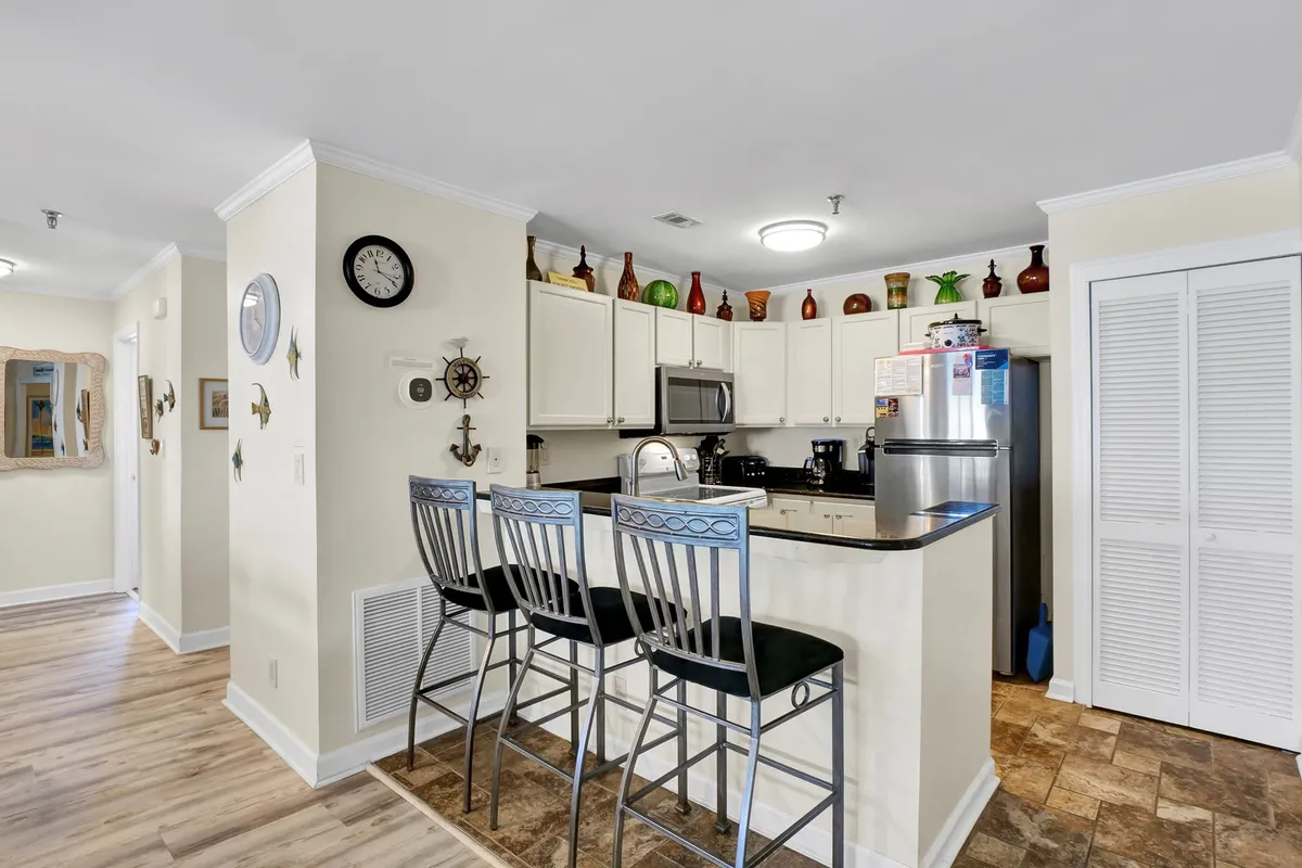A close-up of the kitchen countertop with bar stools tucked underneath, complemented by decorative bottles and a bright, welcoming ambiance. The setup emphasizes casual dining and a relaxed environment where culinary activities can be enjoyed in company.