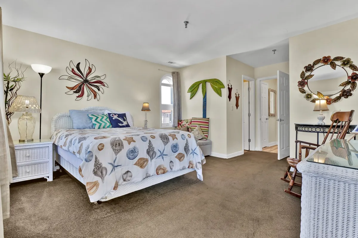 A cheerful, relaxed bedroom scene with a bed dressed in sea-themed bedding, decorative art on the wall, cozy lamps and furniture, and a reading nook. The space is filled with natural light, perfect for restful mornings or winding down at night.